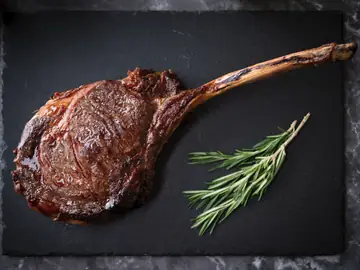 a beef steak on a dark slate. The steak is a tomahawk cut
